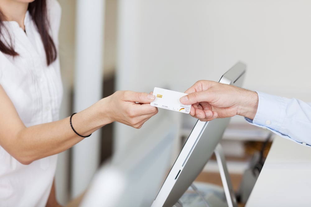 Closeup of receptionist receiving card from male patient in dentist clinic | ESB Professional / Shutterstock