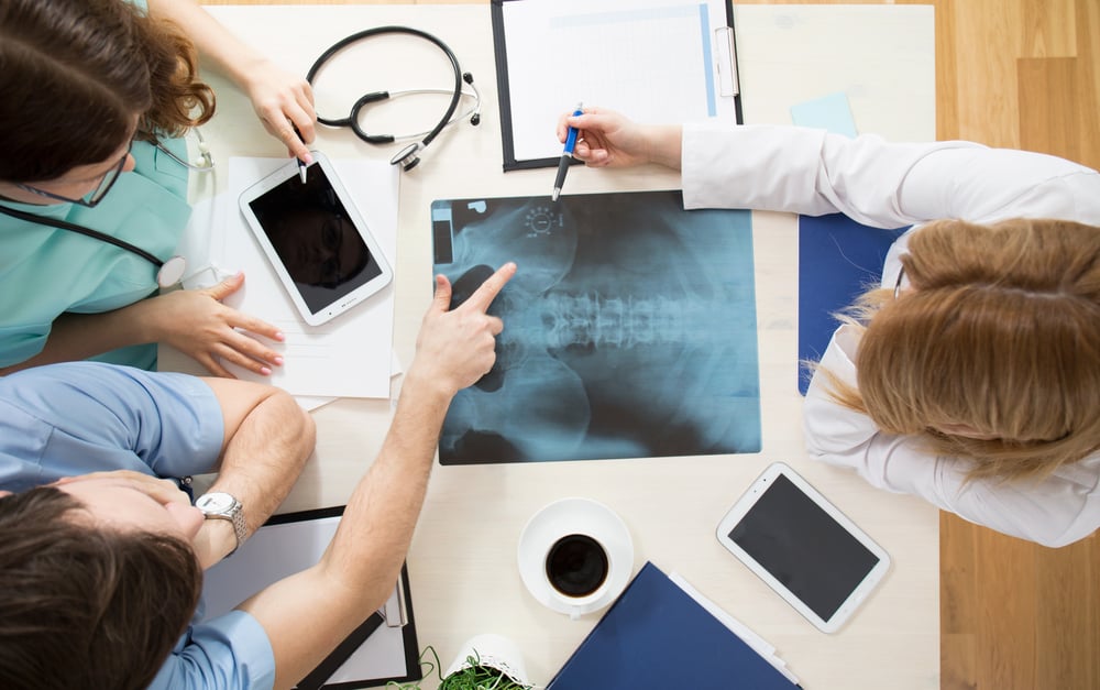 Doctors sitting around the table and interpreting x-ray image | ESB Professional / Shutterstock